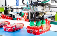 Die Vakuumgreifer handhaben die zerbrechlichen Produkte so schonend wie möglich. Im Hintergrund ist zu sehen, wie das Produktband für die Gruppierung geschwenkt wird.
