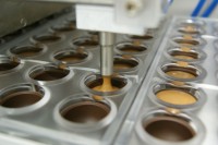 Einfüllen von flüssigem Nougat in Schokoladenhülsen, die durch Kaltstempeln hergestellt wurden.
